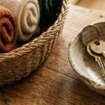 Ultra close-up macro of an autumn entryway drop zone on an oak console with a woven seagrass basket holding rolled wool scarves and a ceramic key dish