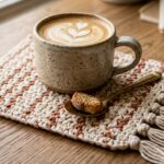 Modern boho cream and terracotta crochet mug rug with fringe tassels holding a ceramic coffee mug