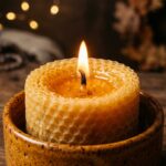 Ultra close-up macro eye-level shot of a pure golden beeswax pillar candle glowing softly with a calm steady flame in an amber ceramic holder