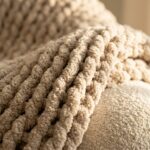 Handmade chunky oatmeal crochet throw blanket draped over cream bouclé armchair