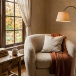 Cozy fall reading nook corner with boucle armchair plaid throw warm lamp and steaming tea