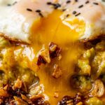 Ultra close-up macro shot of runny egg yolk cascading over seasoned mashed avocado and crispy chili crisp oil