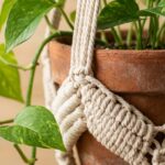 Ultra close-up of handmade crochet plant hanger in natural cotton holding terracotta pot with pothos