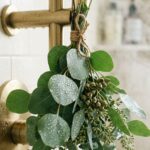Ultra close-up macro eye-level shot of fresh silver dollar eucalyptus bundle tied with jute twine hanging beside a brass shower fixture with gentle steam