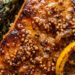 Ultra close-up macro food photography of caramelized honey mustard glazed salmon fillets roasted alongside crisp-tender green asparagus spears on a sheet pan