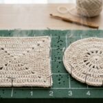 Ultra close-up macro of handmade natural ecru crochet coasters pinned onto a grid blocking board with steam gently rising
