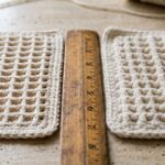 Close-up macro comparison of handmade textured cotton crochet dishcloth after 1 wash versus after 15 wash cycles on travertine workbench