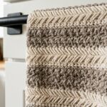 Ultra close-up macro of textured crochet kitchen towel in cream and taupe cotton hanging from oven handle