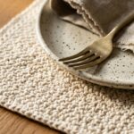 Modern rectangular cream cotton crochet placemat with dinner plate and brass cutlery on oak table