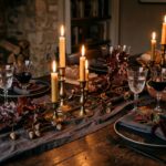 Moody candlelit fall dinner table setting on rustic wood with glowing brass tapers and dark ceramics