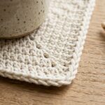 Ultra close-up macro of handmade square crochet coaster with twisted crab stitch border in natural ecru cotton