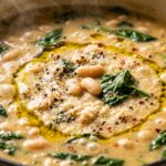 Ultra close-up macro food photography of creamy white bean and spinach soup bubbling in a cast iron Dutch oven with tender beans and vibrant greens