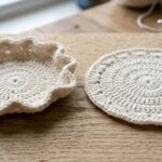 Side by side comparison of a warped bowl curling crochet coaster versus a perfectly flat blocked coaster on oak workbench