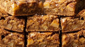Ultra close-up macro food photography of freshly sliced chewy brown butter apple blondies stacked with caramelized cinnamon apples and flaky sea salt