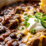 Extreme close-up macro of a chili bar bowl with sharp cheddar and cornbread