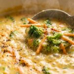 Ultra close-up macro food photography of rich velvety creamy broccoli cheddar soup with tender florets and melted sharp cheese simmering in a Dutch oven