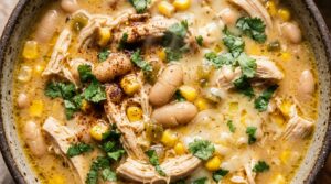 Ultra close-up macro texture of creamy white chicken chili with shredded chicken, white cannellini beans, and melted Monterey Jack cheese