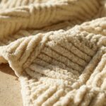 Macro close-up of handcrafted chunky basketweave crochet throw blanket showing raised alternating woven blocks and plush cream yarn texture