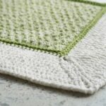 Ultra close-up macro photograph of handcrafted textured cotton crochet bath mat showing raised treble post nubby center and white ribbed border