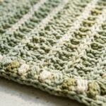 Ultra close-up macro photograph of handcrafted textured cotton crochet kitchen towel showing raised vertical ridges and border puff stitches