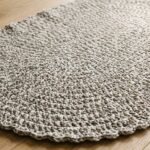 Handcrafted modern oval crochet floor rug in heathered stone grey cotton tube yarn resting on a natural white oak floor