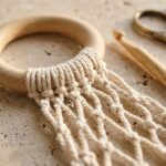 Close-up macro of crochet plant hammock beechwood ring wrapped with unbleached cotton cord and diamond mesh lattice on travertine workbench