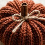 Macro close-up of handmade terracotta ribbed crochet pumpkin with cinnamon stick stem and jute bow on travertine stone