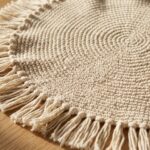 Handcrafted round crochet placemat in natural ecru cotton yarn showing spiral single crochet texture on a white oak dining table