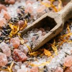 Coarse pink Himalayan salt crystals, translucent Epsom salt granules, and dried French lavender buds with wooden scoop