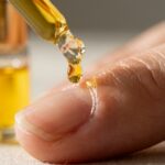 Ultra close-up macro of golden jojoba cuticle oil in glass rollerball bottle with oil droplet on fingernail