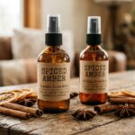 Close-up of amber glass spray bottles with fine mist nozzles, rustic kraft labels, cinnamon bark sticks, and dried orange slices on a weathered wooden table