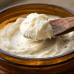 Ultra close-up macro of freshly whipped fluffy ivory shea body butter with soft peaks in glass jar