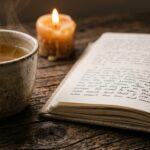 Ceramic mug of chamomile tea, open linen journal, and glowing beeswax candle on wooden table in warm evening light