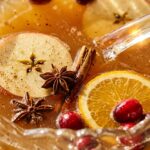 Extreme close-up macro of an ornate crystal punch bowl filled with sparkling autumn spiced cider punch with floating Honeycrisp apples, cranberries, and cinnamon sticks