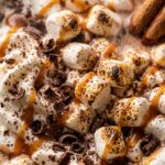 Ultra close-up macro texture of hot chocolate in ceramic mug topped with whipped cream, mini marshmallows, chocolate shavings, and caramel drizzle