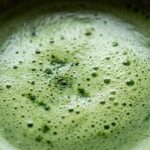 Ultra close-up macro texture of freshly whisked vibrant emerald green matcha tea with micro-foam bubbles in ceramic bowl