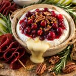 Extreme close-up macro of a holiday Thanksgiving appetizer board with baked brie wheel topped with spiced cranberries, pecans, seeded crackers, and pear slices