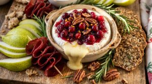 Extreme close-up macro of a holiday Thanksgiving appetizer board with baked brie wheel topped with spiced cranberries, pecans, seeded crackers, and pear slices