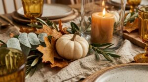 Extreme close-up macro of a Thanksgiving centerpiece with silver dollar eucalyptus, miniature white pumpkins, and warm glowing candles